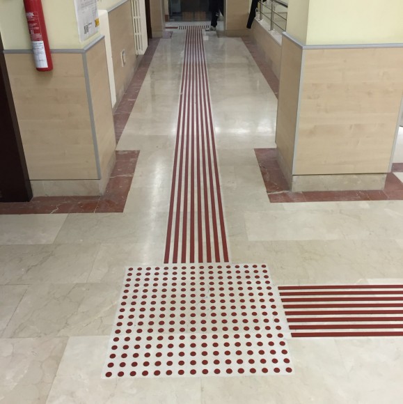 Cruce de direcciones en un pasillo. En el suelo hay un pavimento tactovisual con tiras en el recorrido del pasillo y con tetones en el cruce de direcciones. Tiene buen contraste.. Acceso a la galería. Abre nueva ventana